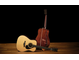 Two acoustic guitars on a wooden floor with a black background. One stands upright, showcasing its distinctive wood grain of Guatemalan rosewood on its back and sides, while the other lies in front, displaying the Adirondack spruce top.